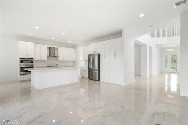 kitchen featuring white cabinets, french doors, a center island with sink, wall chimney exhaust hood, and stainless steel appliances