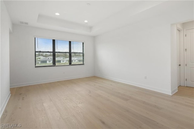 unfurnished room featuring light wood-type flooring and a raised ceiling