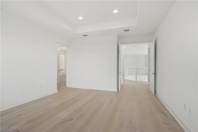 unfurnished room with light wood-type flooring and a tray ceiling