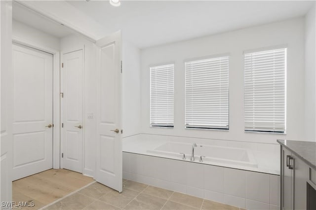 bathroom with a relaxing tiled tub, tile patterned flooring, and vanity