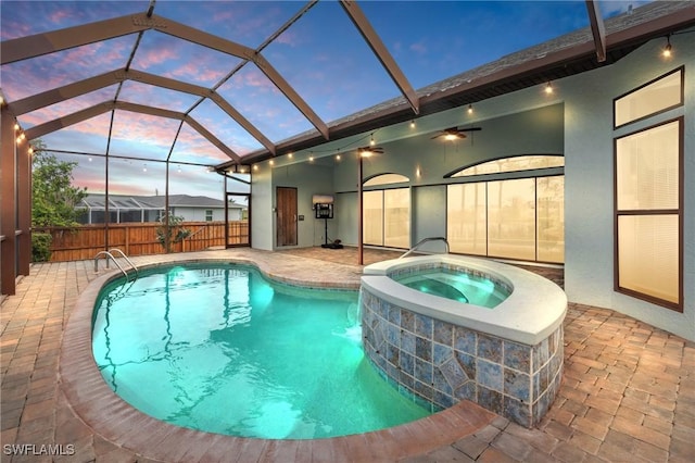 pool at dusk with an in ground hot tub, glass enclosure, and a patio area