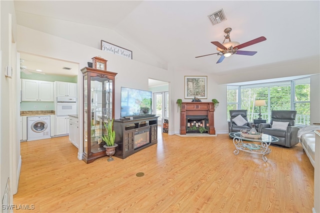 living room featuring washer / clothes dryer, ceiling fan, light hardwood / wood-style floors, and vaulted ceiling