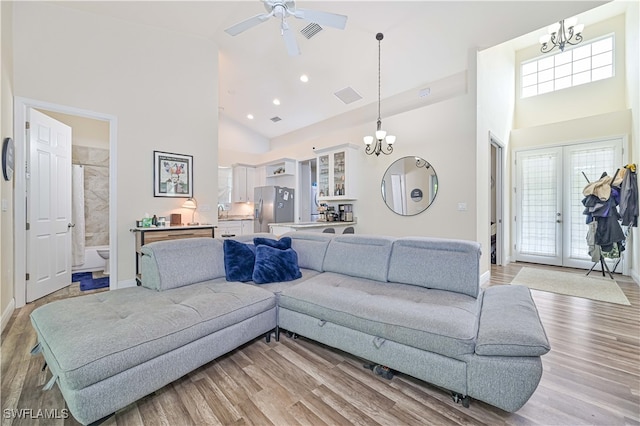 living room featuring ceiling fan with notable chandelier, a towering ceiling, and light hardwood / wood-style floors