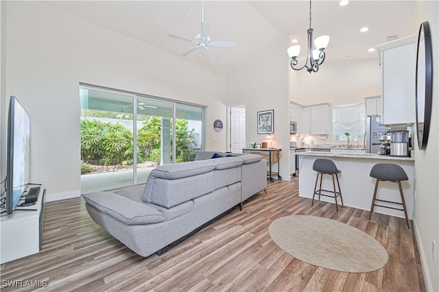 living room with ceiling fan with notable chandelier, light wood-type flooring, and high vaulted ceiling