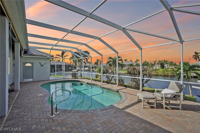 pool at dusk featuring a water view, glass enclosure, and a patio area