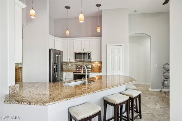 kitchen with a high ceiling, kitchen peninsula, decorative backsplash, white cabinetry, and stainless steel appliances