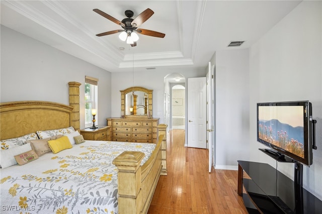 bedroom featuring connected bathroom, ceiling fan, a raised ceiling, light hardwood / wood-style floors, and ornamental molding