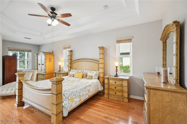 bedroom with multiple windows, a tray ceiling, ceiling fan, and light hardwood / wood-style floors