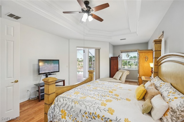 bedroom featuring access to outside, light hardwood / wood-style flooring, ceiling fan, ornamental molding, and a tray ceiling