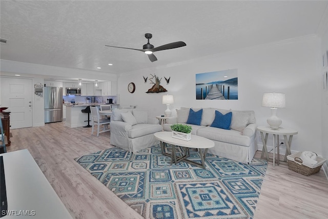 living room with light wood-type flooring, a textured ceiling, ornamental molding, and ceiling fan