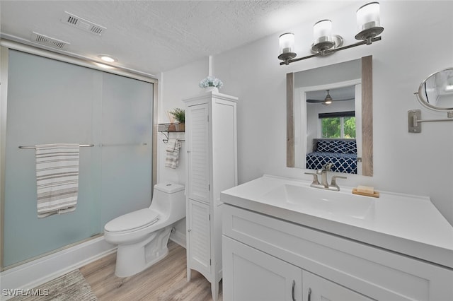 bathroom with a textured ceiling, hardwood / wood-style flooring, ceiling fan, vanity, and toilet