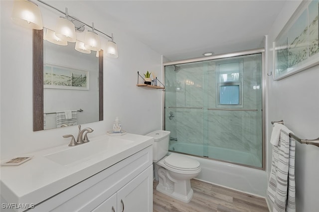 full bathroom featuring hardwood / wood-style floors, bath / shower combo with glass door, vanity, and toilet