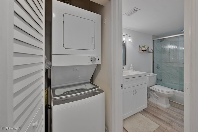 clothes washing area featuring stacked washer and clothes dryer and light hardwood / wood-style flooring