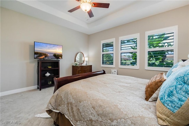 bedroom featuring light carpet, multiple windows, a raised ceiling, and ceiling fan