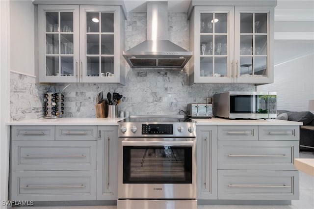 kitchen with gray cabinets, decorative backsplash, appliances with stainless steel finishes, and wall chimney range hood