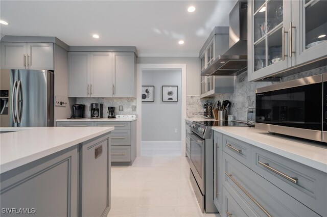 kitchen with gray cabinetry, stainless steel appliances, wall chimney range hood, and decorative backsplash