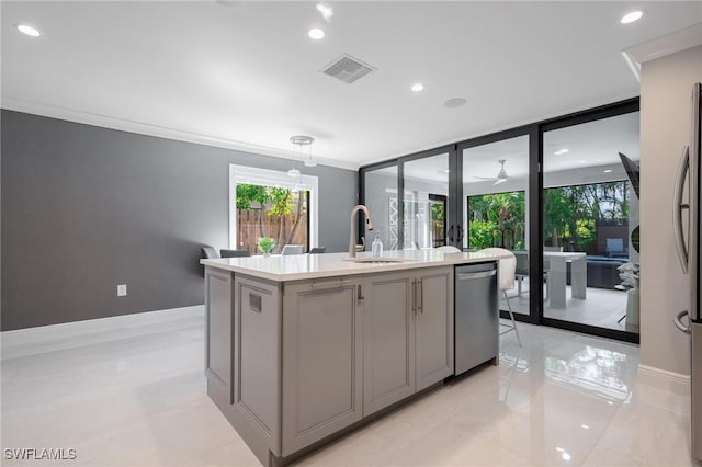 kitchen with hanging light fixtures, stainless steel appliances, a center island with sink, sink, and gray cabinets