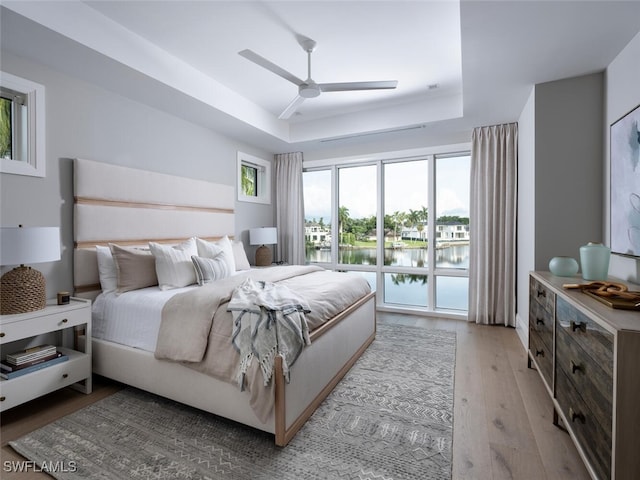 3131 Gin Ln, Naples, FL 34102 - bedroom featuring a raised ceiling, a water view, light wood-style flooring, and ceiling fan
