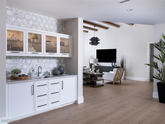 bar with sink, white cabinets, beamed ceiling, light wood-type flooring, and decorative backsplash