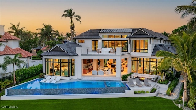 back house at dusk with a balcony, a patio, an outdoor hangout area, and a yard