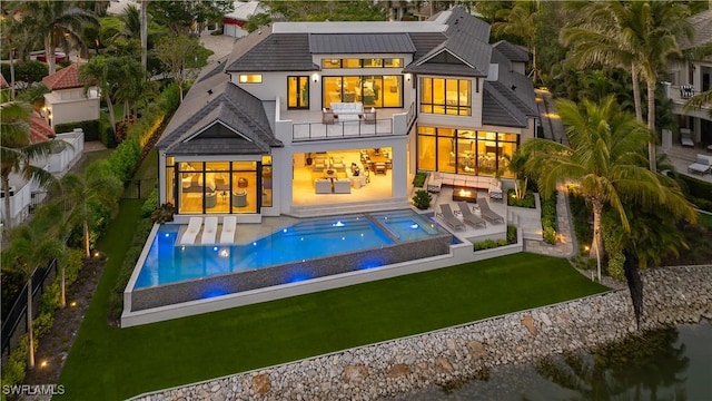 rear view of property with a lawn, a balcony, exterior kitchen, a patio, and a swimming pool with hot tub