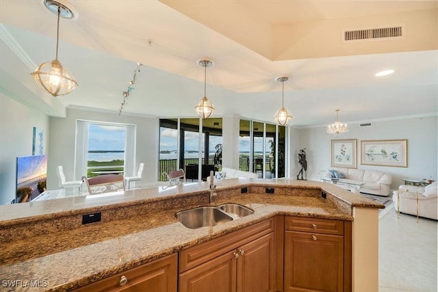 kitchen with light stone counters, crown molding, hanging light fixtures, and sink