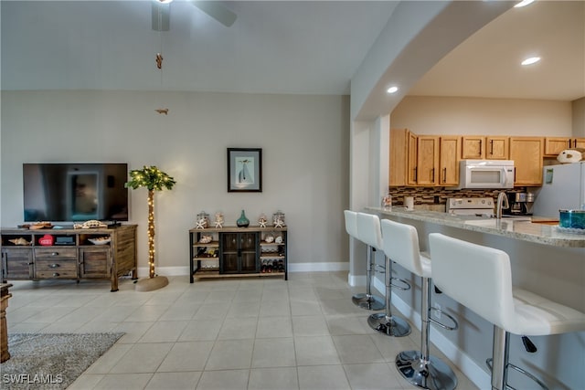 kitchen with light stone counters, light tile patterned floors, ceiling fan, white appliances, and backsplash