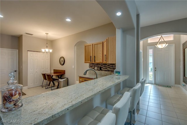 kitchen featuring light tile patterned flooring, tasteful backsplash, a kitchen bar, hanging light fixtures, and light stone counters