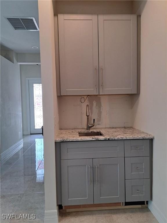 kitchen with decorative backsplash, gray cabinets, light stone countertops, and sink