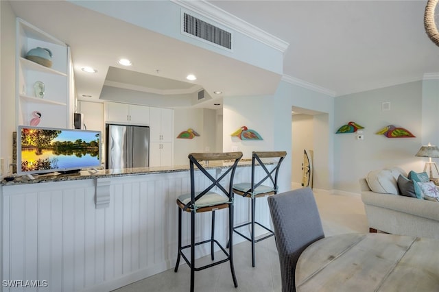 kitchen with high end refrigerator, dark stone countertops, white cabinetry, kitchen peninsula, and crown molding