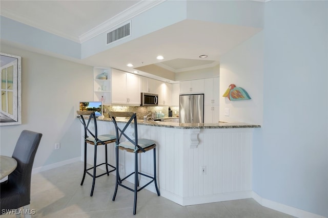 kitchen with light tile patterned flooring, kitchen peninsula, stone counters, white cabinetry, and appliances with stainless steel finishes