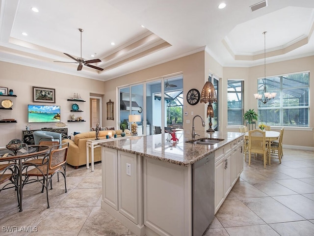 kitchen with ceiling fan with notable chandelier, dishwasher, a tray ceiling, a center island with sink, and sink