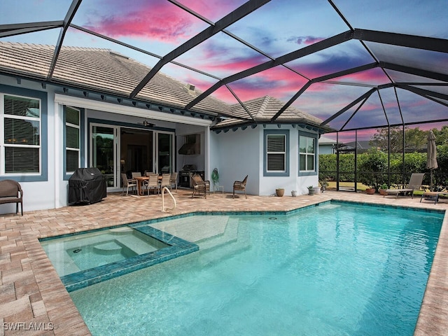 pool at dusk featuring glass enclosure, area for grilling, ceiling fan, and a patio area