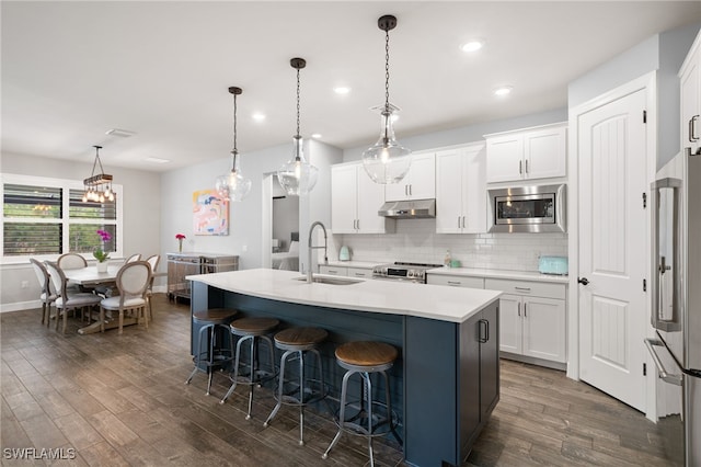 kitchen featuring a kitchen island with sink, stainless steel appliances, sink, decorative light fixtures, and white cabinets