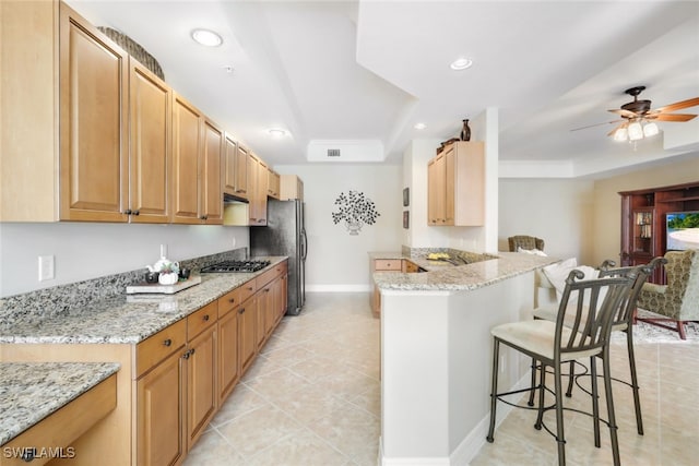 kitchen with a breakfast bar area, a tray ceiling, kitchen peninsula, a barn door, and light stone countertops