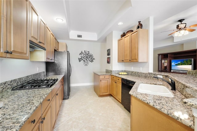 kitchen featuring stainless steel gas stovetop, black dishwasher, sink, ceiling fan, and a tray ceiling