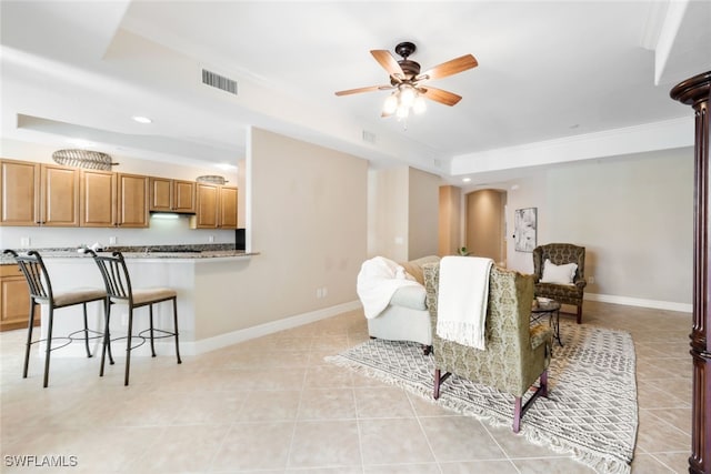 tiled living room with ornamental molding, a raised ceiling, and ceiling fan