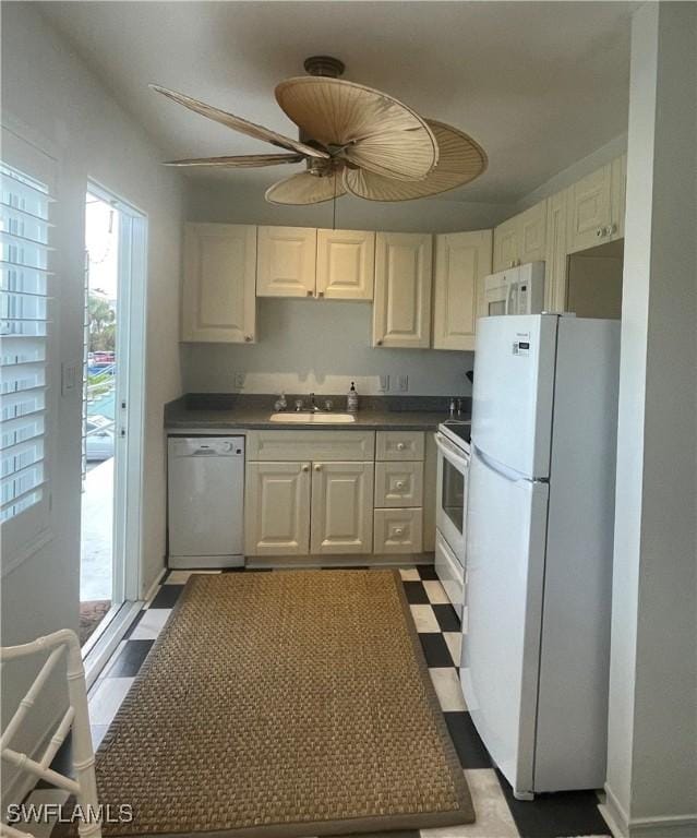 kitchen featuring white appliances, a sink, white cabinets, dark countertops, and dark floors