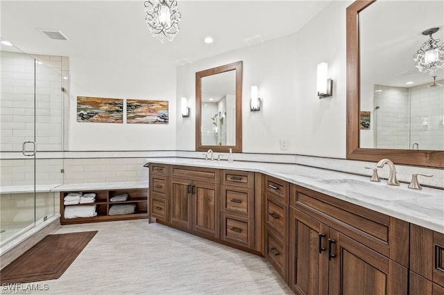 full bathroom with visible vents, an inviting chandelier, double vanity, a stall shower, and a sink