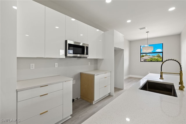 kitchen with pendant lighting, white cabinets, sink, light hardwood / wood-style flooring, and light stone counters