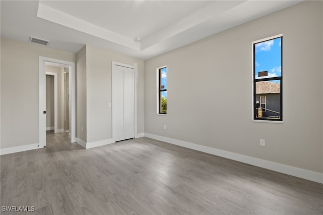 unfurnished bedroom with light hardwood / wood-style floors, a closet, and a tray ceiling