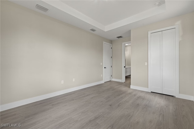 unfurnished bedroom with a raised ceiling, a closet, and light hardwood / wood-style flooring