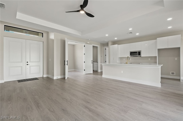 unfurnished living room with a tray ceiling, ceiling fan, light hardwood / wood-style flooring, and sink