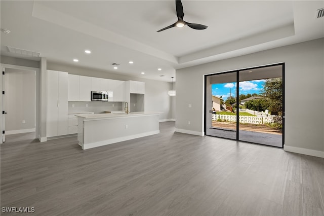 unfurnished living room with a raised ceiling, ceiling fan, sink, and light hardwood / wood-style floors