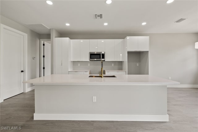 kitchen with sink, white cabinetry, a kitchen island with sink, and light wood-type flooring