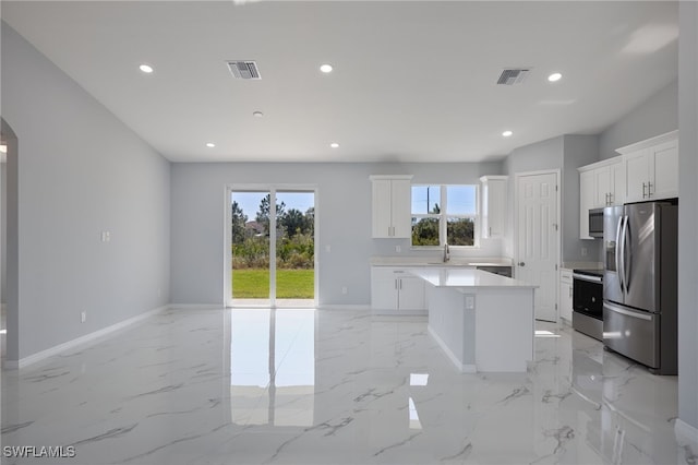 kitchen with appliances with stainless steel finishes, white cabinetry, a kitchen island, and a healthy amount of sunlight