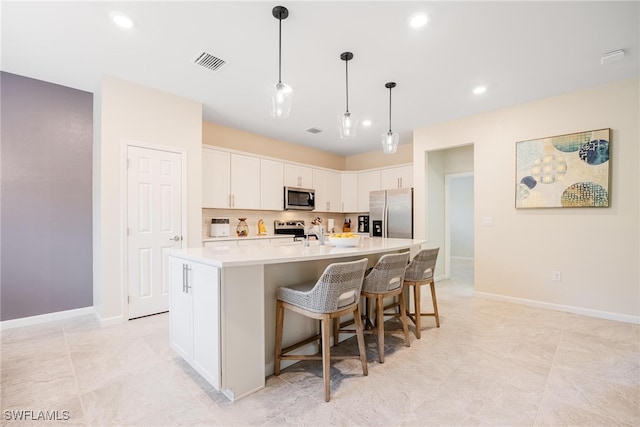 kitchen featuring a kitchen island with sink, a breakfast bar area, white cabinetry, decorative backsplash, and appliances with stainless steel finishes