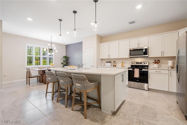 kitchen featuring white cabinets, a kitchen island with sink, stainless steel appliances, and hanging light fixtures