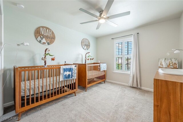 carpeted bedroom with baseboards, a nursery area, and ceiling fan