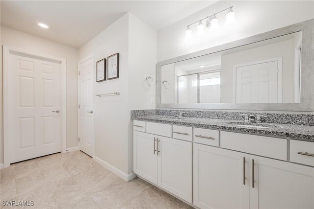 bathroom with a sink, baseboards, walk in shower, and double vanity